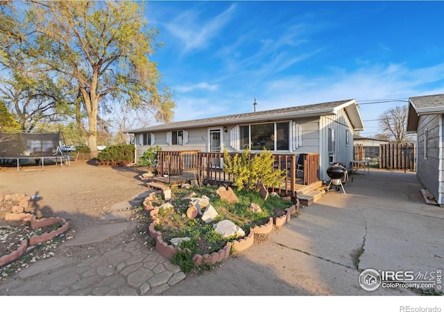 ranch-style home featuring a deck, fence, and a trampoline