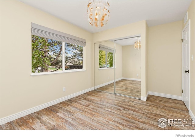 unfurnished bedroom with baseboards, a closet, wood finished floors, and a notable chandelier