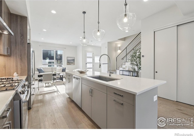 kitchen with appliances with stainless steel finishes, a sink, light countertops, light wood finished floors, and open floor plan