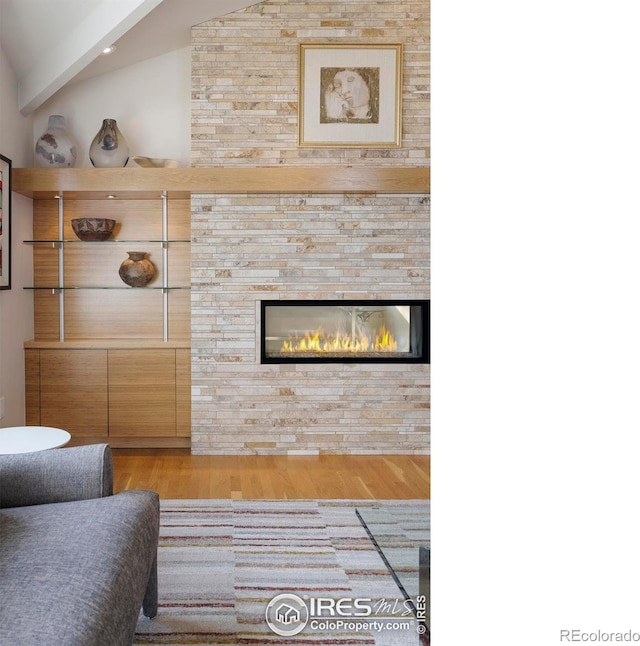 living room featuring a large fireplace, vaulted ceiling, and wood finished floors