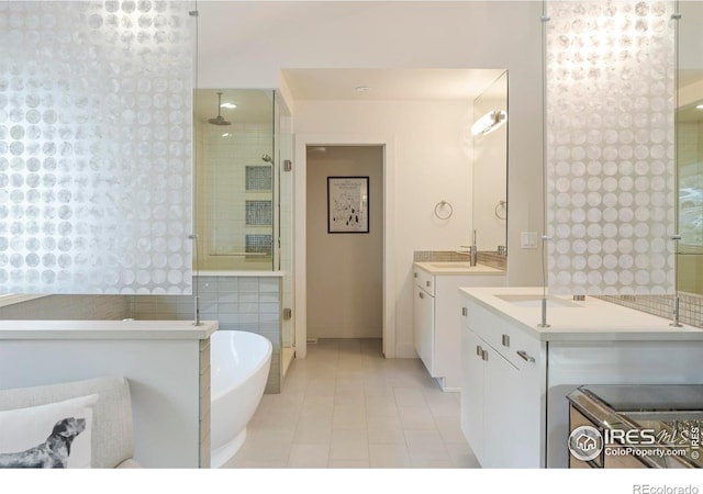 bathroom with tile patterned flooring, a shower stall, two vanities, a sink, and a soaking tub