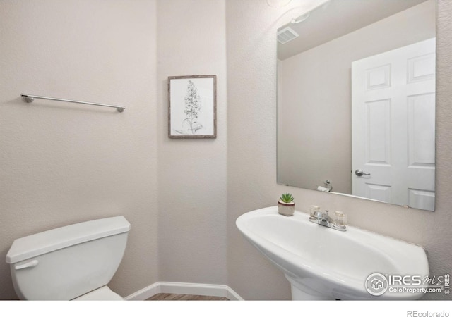 half bath featuring visible vents, wood finished floors, toilet, baseboards, and a sink