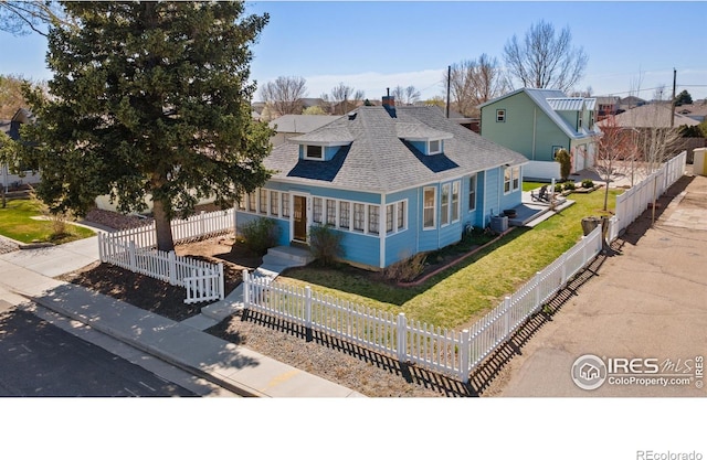 view of front of house featuring roof with shingles, a fenced front yard, central AC, and a front yard