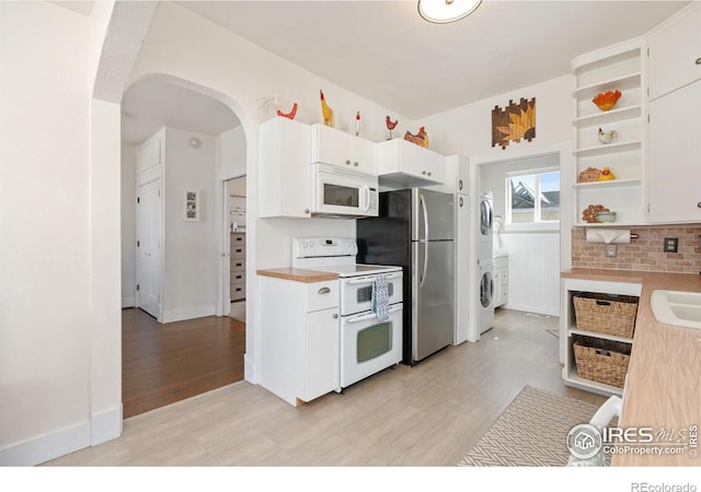 kitchen featuring open shelves, white appliances, arched walkways, stacked washing maching and dryer, and light wood-style flooring