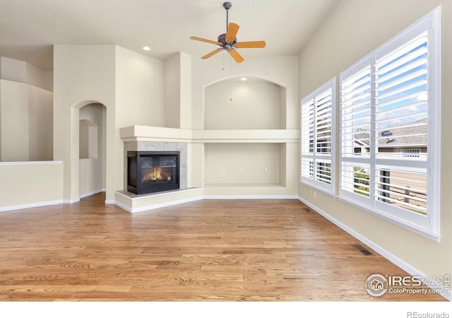 unfurnished living room featuring a ceiling fan, visible vents, plenty of natural light, and wood finished floors