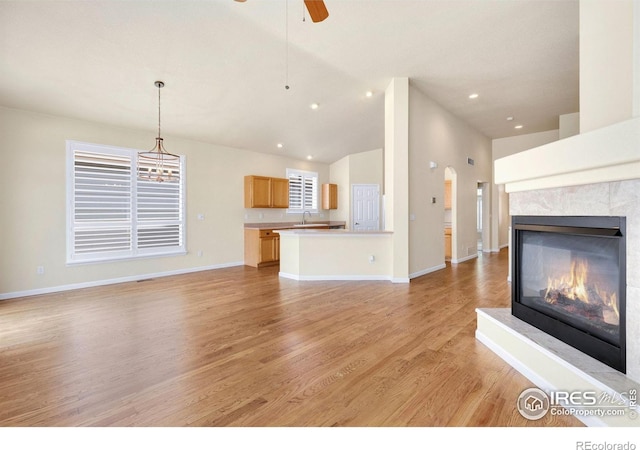 unfurnished living room with light wood-style floors, baseboards, ceiling fan, a tile fireplace, and a sink