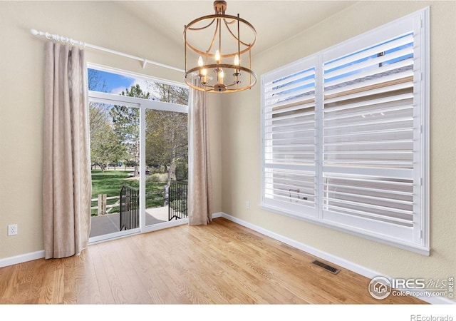 unfurnished dining area featuring an inviting chandelier, baseboards, wood finished floors, lofted ceiling, and visible vents