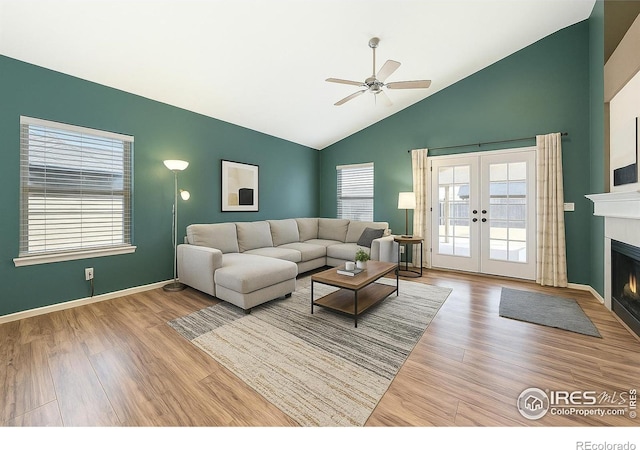 living room with wood finished floors, ceiling fan, a lit fireplace, high vaulted ceiling, and french doors