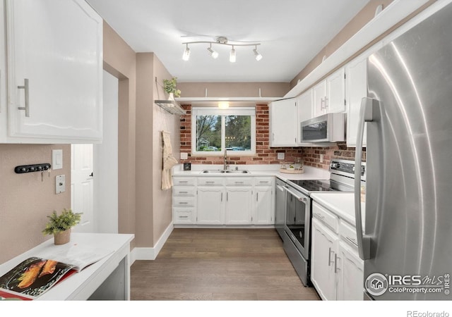 kitchen with appliances with stainless steel finishes, wood finished floors, a sink, light countertops, and white cabinetry