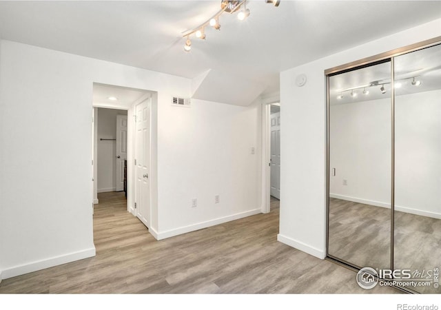 unfurnished bedroom with baseboards, visible vents, track lighting, and wood finished floors