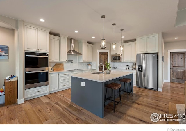 1603 Plank Ln, Fort Collins, CO 80524 - kitchen with wall chimney range hood, a kitchen bar, white cabinets, light wood-style flooring, and stainless steel appliances