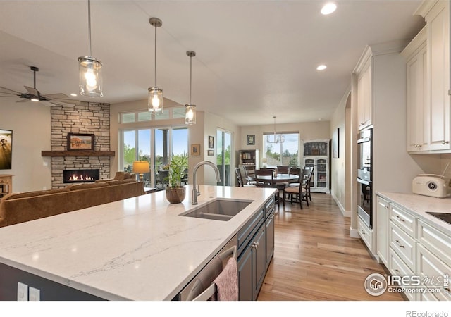 1603 Plank Ln, Fort Collins, CO 80524 - kitchen with ceiling fan, a stone fireplace, light wood-type flooring, a sink, and white cabinetry