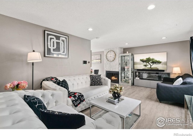 living room featuring a textured ceiling, a fireplace, recessed lighting, and wood finished floors