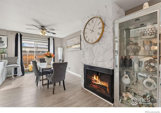dining space with wood finished floors, a fireplace, baseboards, a textured ceiling, and a ceiling fan