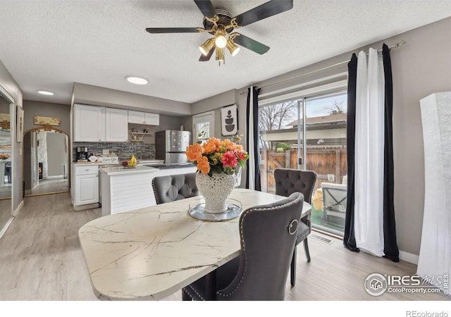 dining area with ceiling fan, a textured ceiling, baseboards, and light wood-style flooring