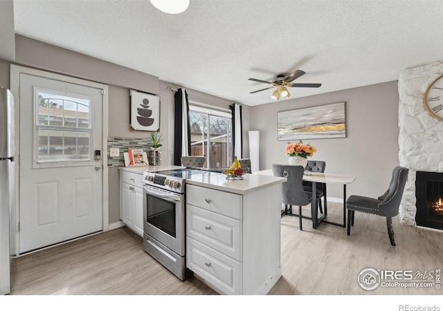 kitchen with a peninsula, light countertops, white cabinets, light wood finished floors, and appliances with stainless steel finishes