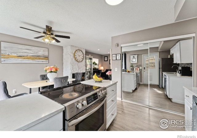 kitchen with white cabinets, stainless steel range with electric cooktop, light wood finished floors, light countertops, and a ceiling fan