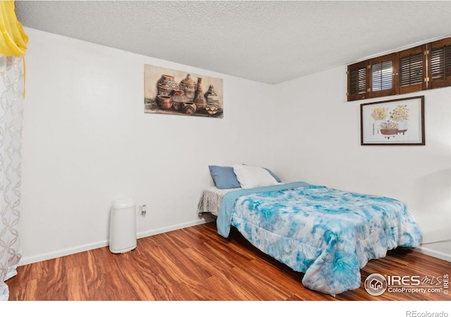 bedroom featuring baseboards, a textured ceiling, and wood finished floors