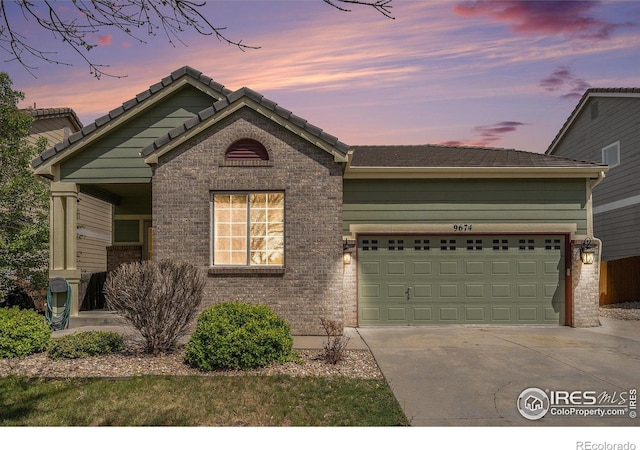 view of front of home with brick siding, an attached garage, driveway, and a tiled roof