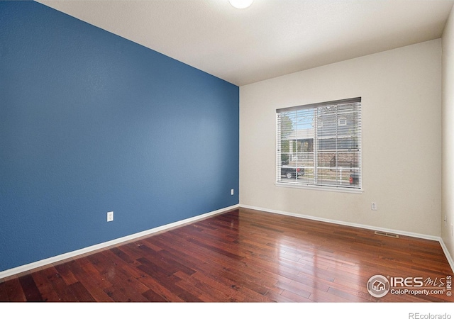 empty room with baseboards, visible vents, and wood finished floors