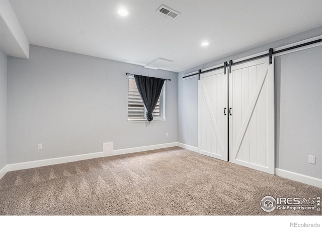 unfurnished bedroom with carpet floors, a barn door, visible vents, and recessed lighting