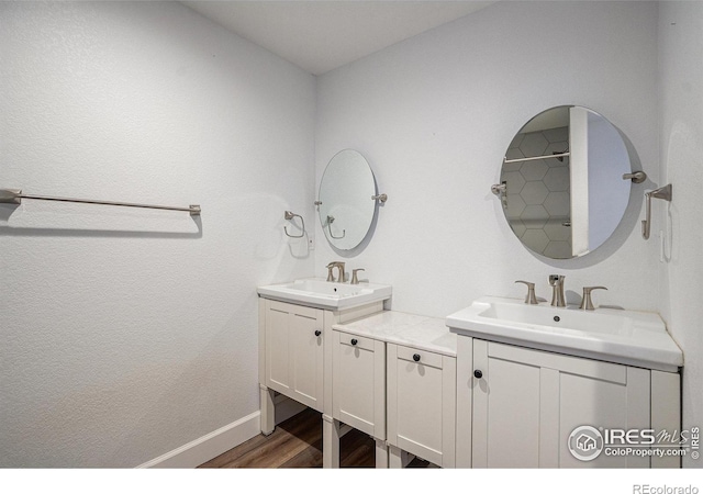 full bathroom featuring a sink, baseboards, wood finished floors, and two vanities