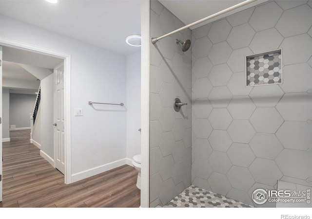 bathroom featuring baseboards, a tile shower, toilet, and wood finished floors
