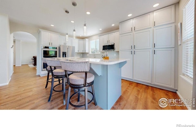 kitchen with appliances with stainless steel finishes, arched walkways, white cabinetry, a breakfast bar area, and light countertops