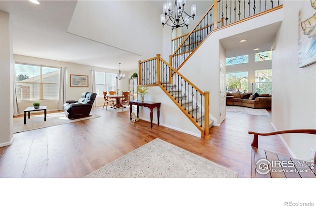 stairs featuring a chandelier, wood finished floors, a towering ceiling, and baseboards