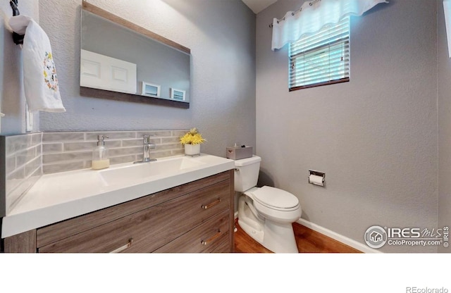 half bathroom with backsplash, toilet, baseboards, vanity, and wood finished floors
