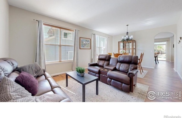 living area with arched walkways, a chandelier, light wood finished floors, and baseboards