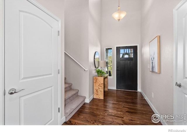 foyer featuring baseboards, stairs, a towering ceiling, and dark wood-type flooring