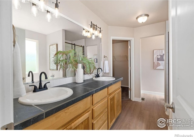 bathroom with double vanity, wood finished floors, a walk in closet, and a sink