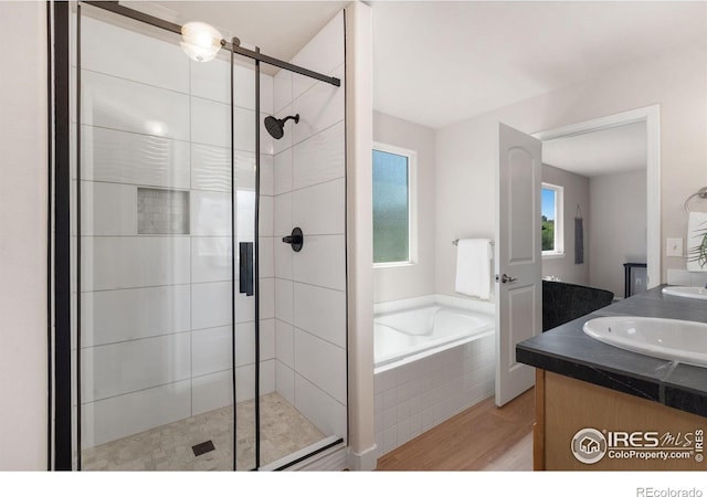 full bath featuring a sink, a shower stall, a garden tub, double vanity, and wood finished floors