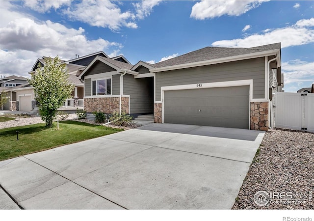 view of front of property with a front lawn, stone siding, a gate, an attached garage, and driveway