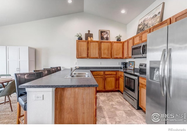 kitchen with dark countertops, a breakfast bar, high vaulted ceiling, a sink, and appliances with stainless steel finishes