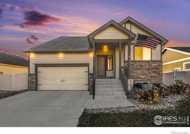 view of front of house with fence, driveway, stone siding, and a garage