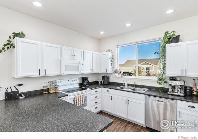 kitchen featuring white appliances, white cabinetry, dark countertops, and a sink