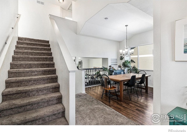 dining area featuring visible vents, vaulted ceiling, wood finished floors, a chandelier, and stairs
