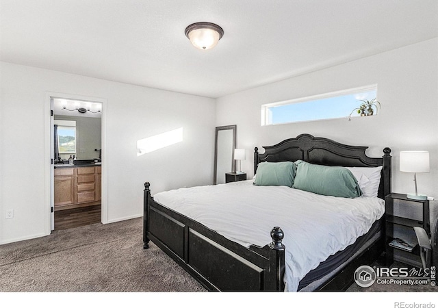 bedroom with dark colored carpet, baseboards, and ensuite bathroom