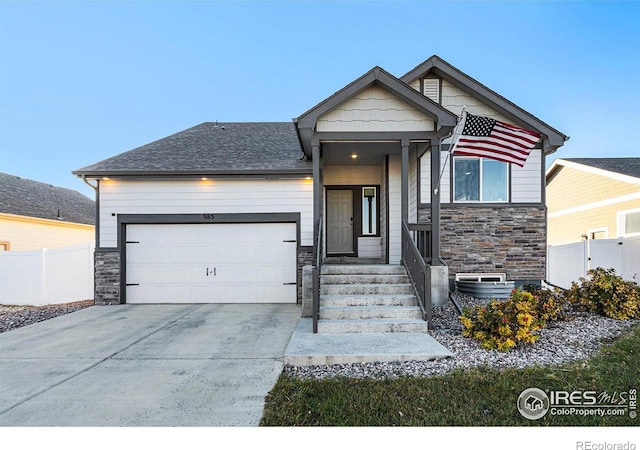 craftsman-style house featuring a garage, fence, driveway, and stone siding