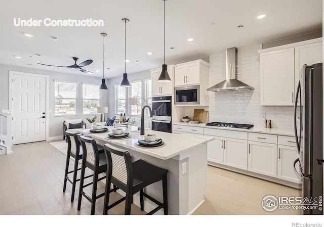 kitchen featuring light countertops, wall chimney exhaust hood, tasteful backsplash, a ceiling fan, and appliances with stainless steel finishes