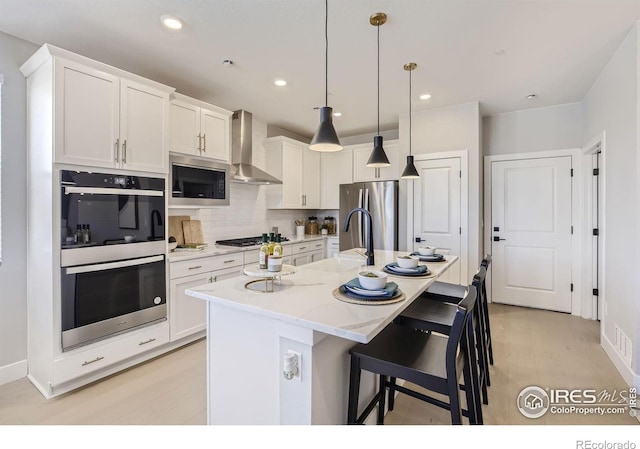 kitchen featuring wall chimney range hood, white cabinets, a breakfast bar, a sink, and stainless steel appliances