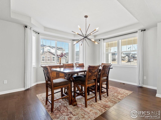 dining room featuring a raised ceiling, baseboards, dark wood-style floors, and a notable chandelier