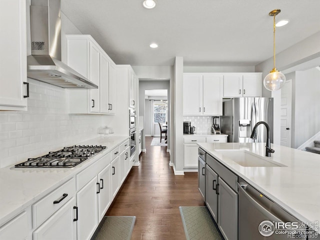 kitchen with dark wood-style flooring, appliances with stainless steel finishes, a sink, gray cabinets, and wall chimney exhaust hood