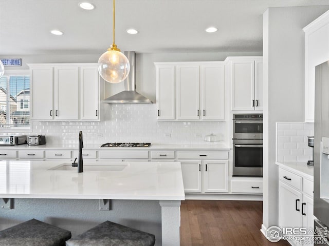 kitchen featuring wall chimney range hood, a kitchen bar, decorative backsplash, and light countertops