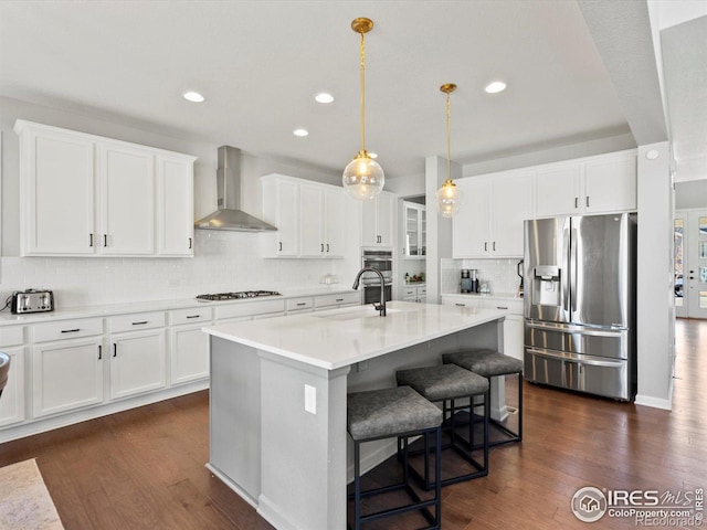 kitchen featuring dark wood-type flooring, wall chimney exhaust hood, tasteful backsplash, a sink, and appliances with stainless steel finishes