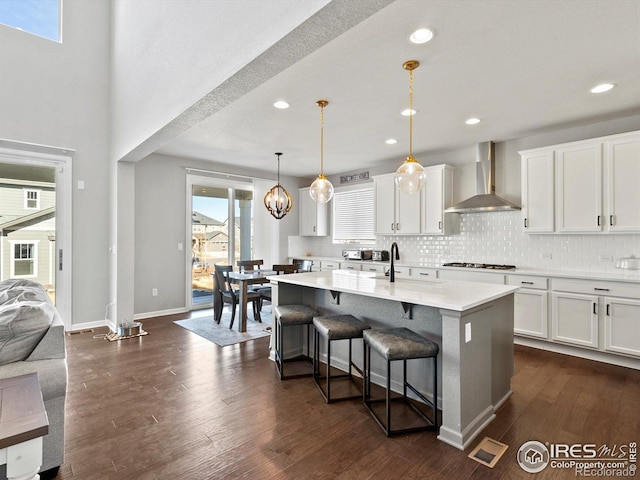 kitchen with white cabinets, a breakfast bar, light countertops, wall chimney exhaust hood, and gas stovetop