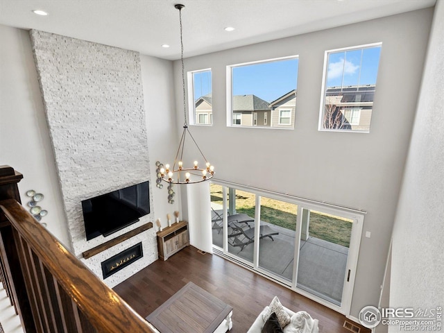 living area with a high ceiling, a notable chandelier, a fireplace, recessed lighting, and wood finished floors