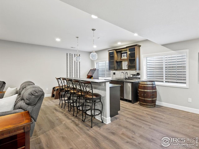 kitchen with a kitchen bar, light wood-type flooring, a sink, baseboards, and glass insert cabinets